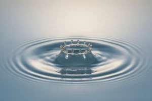 Single droplet hits calm water, ripples expand on neutral background, symbolizing employee advocacy impact.